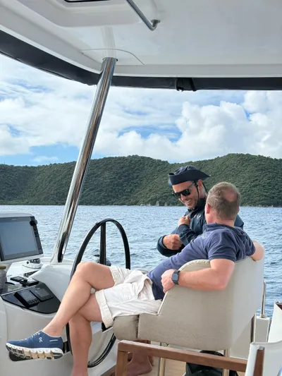 Jdmontt Yacht Photos Pics Two people conversing on a 2024 Lagoon 55 yacht, with scenic ocean and hills in the background.
