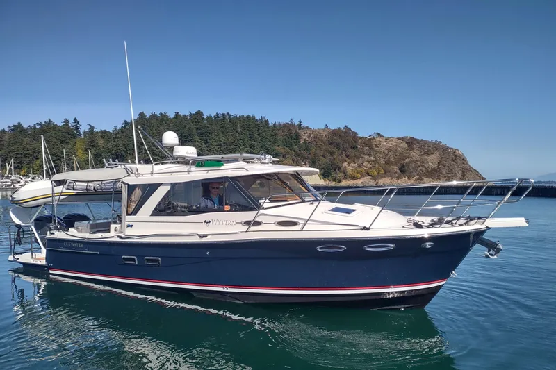 Wyvern Yacht Photos Pics 2020 Cutwater C-32 Coupe boat cruising near a rocky shoreline under clear blue skies.