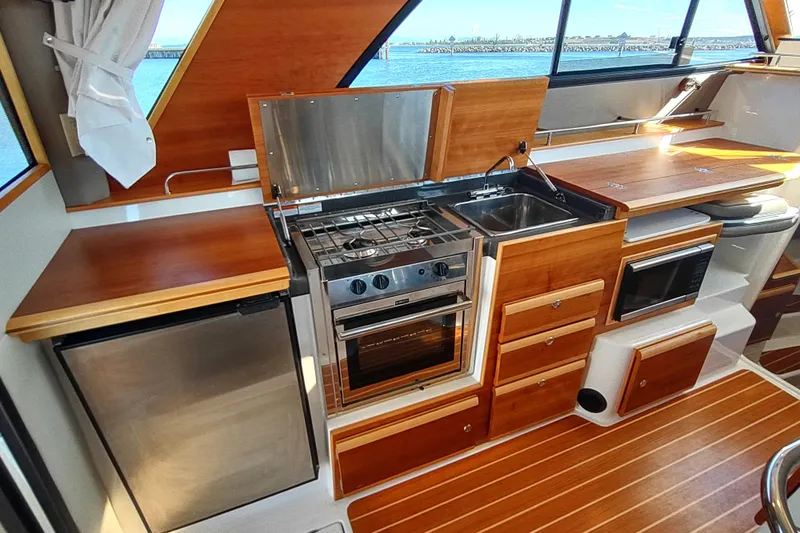 Wyvern Yacht Photos Pics 2020 Cutwater C-32 Coupe kitchen with stove, sink, fridge, and wooden cabinetry.
