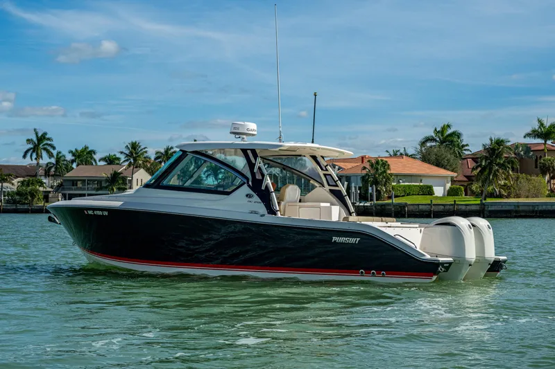  Yacht Photos Pics 2017 Pursuit DC 295 Dual Console boat on water, with palm trees and houses in background.