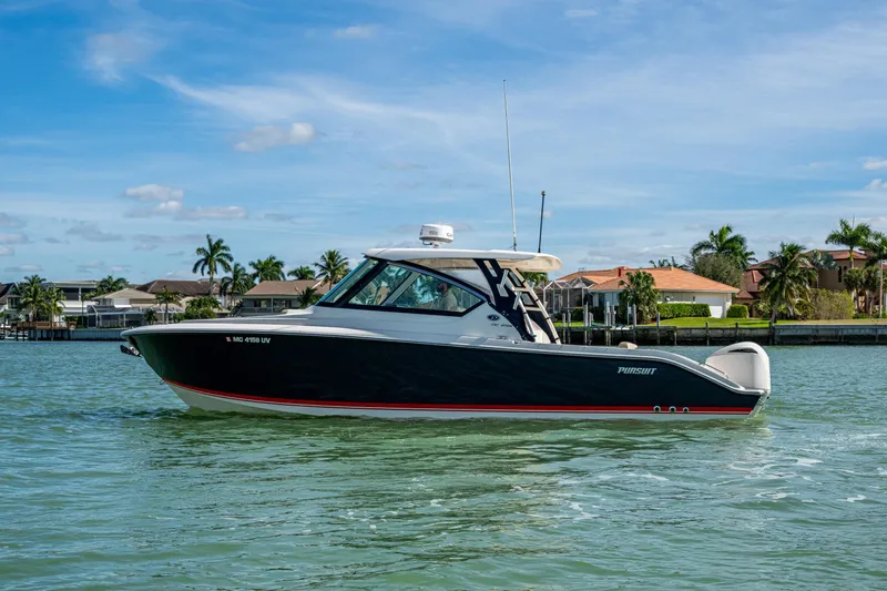  Yacht Photos Pics 2017 Pursuit DC 295 Dual Console boat on calm water, with houses and palm trees in the background.
