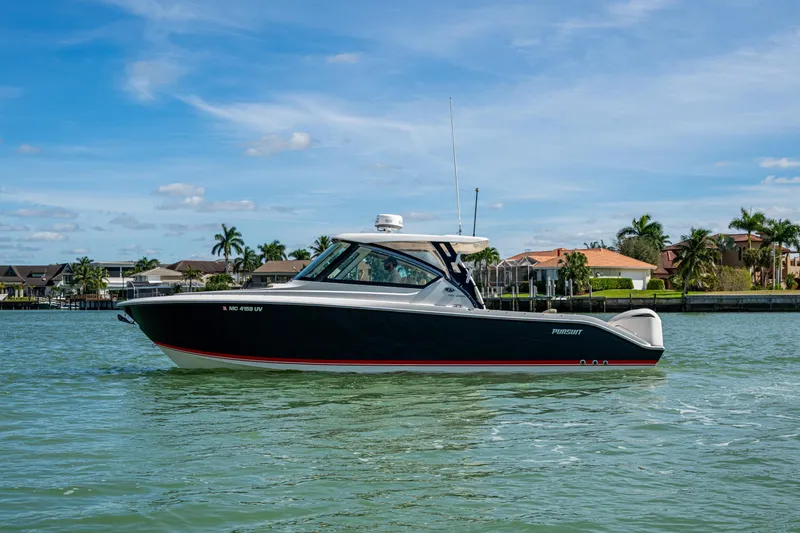  Yacht Photos Pics 2017 Pursuit DC 295 Dual Console boat cruising on a sunny day near waterfront homes.