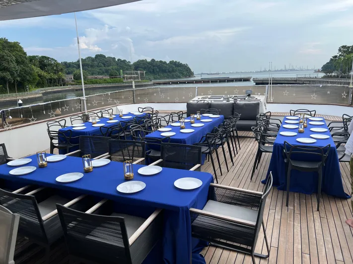  Yacht Photos Pics Outdoor dining setup on 2012 Superyacht 128, featuring blue tablecloths and scenic waterfront view.