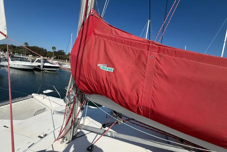 Next Of Kin Yacht Photos Pics Red sail cover on Leopard 38 catamaran, docked in marina, clear blue sky.
