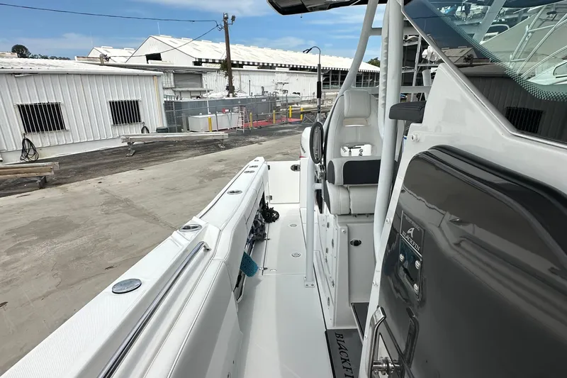  Yacht Photos Pics 2021 Blackfin 332 CC boat interior, featuring helm and seating, docked near industrial buildings.