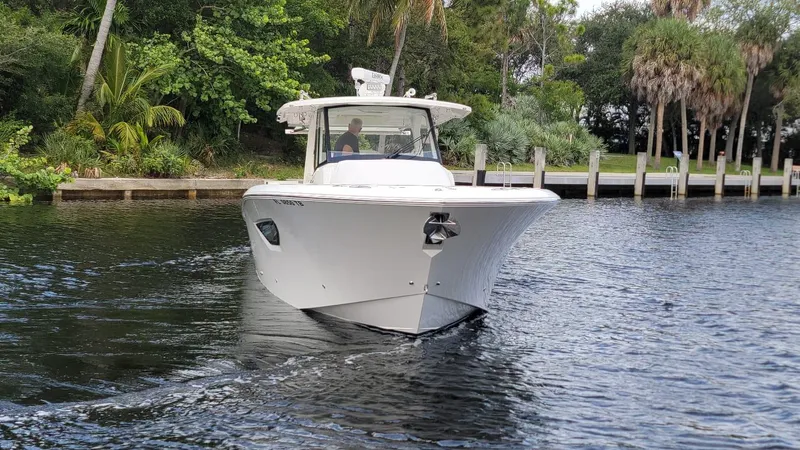  Yacht Photos Pics 2021 Pursuit S 378 Sport boat cruising on a calm river near lush greenery.
