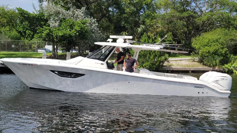  Yacht Photos Pics 2021 Pursuit S 378 Sport boat on a calm river, surrounded by lush greenery.