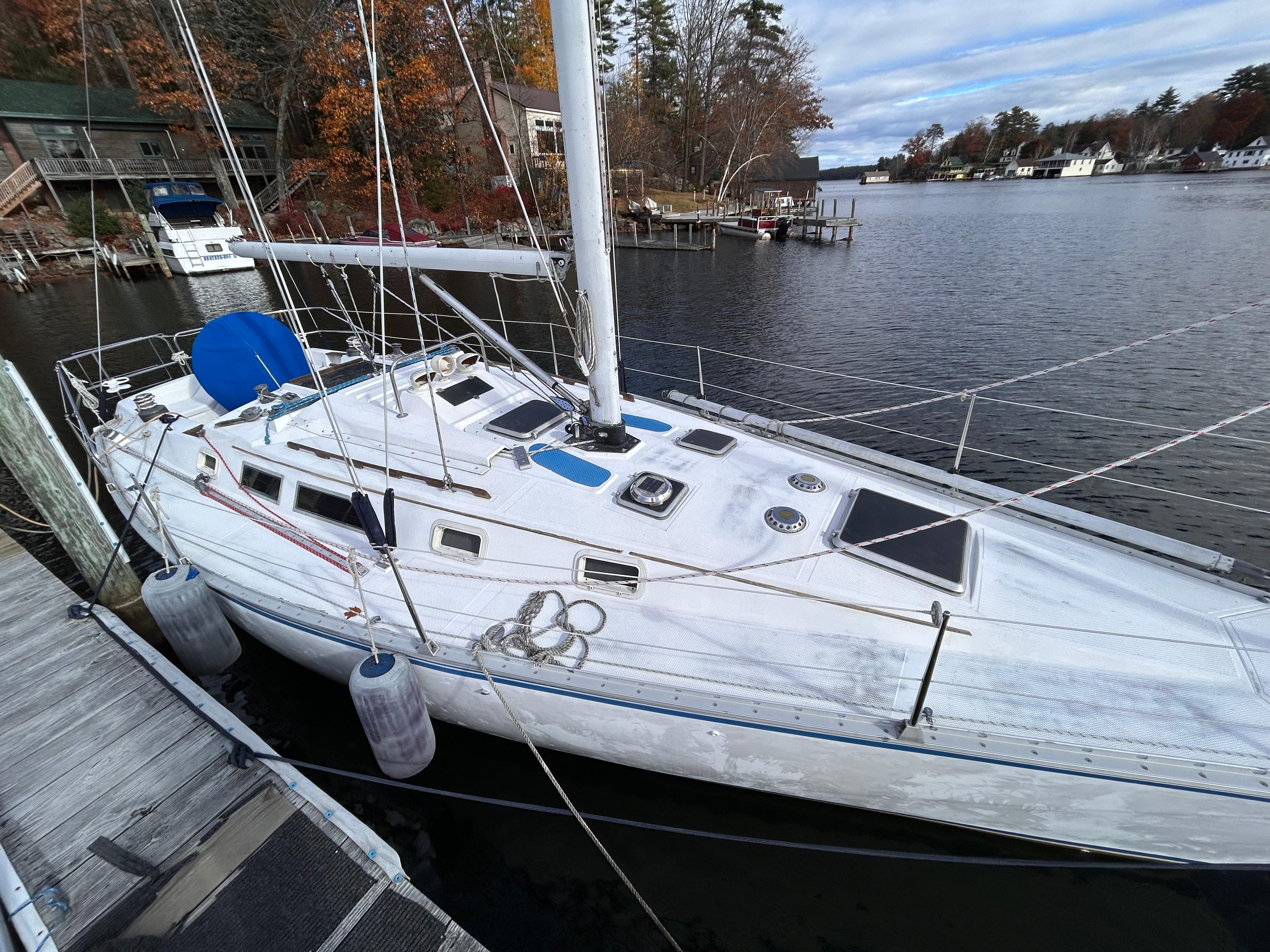1983 Hunter 34 sailboat docked on a calm lake with autumn trees in the background.