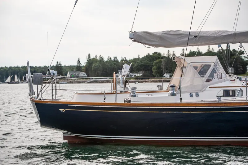 Hera Yacht Photos Pics Hinckley Sou'wester 42 Sloop, 1994, sailing on calm waters near a forested shoreline.