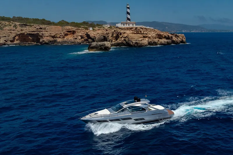 Polar Yacht Photos Pics 2023 Pershing 5x yacht cruising near rocky coastline with lighthouse in background.