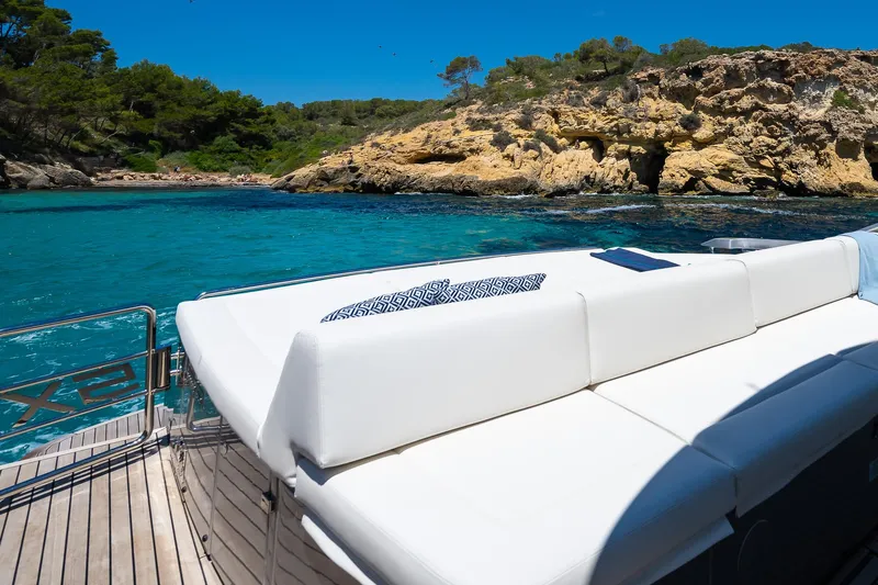 Polar Yacht Photos Pics Luxurious 2023 Pershing 5x yacht with sunbed, turquoise waters, and rocky coastline.