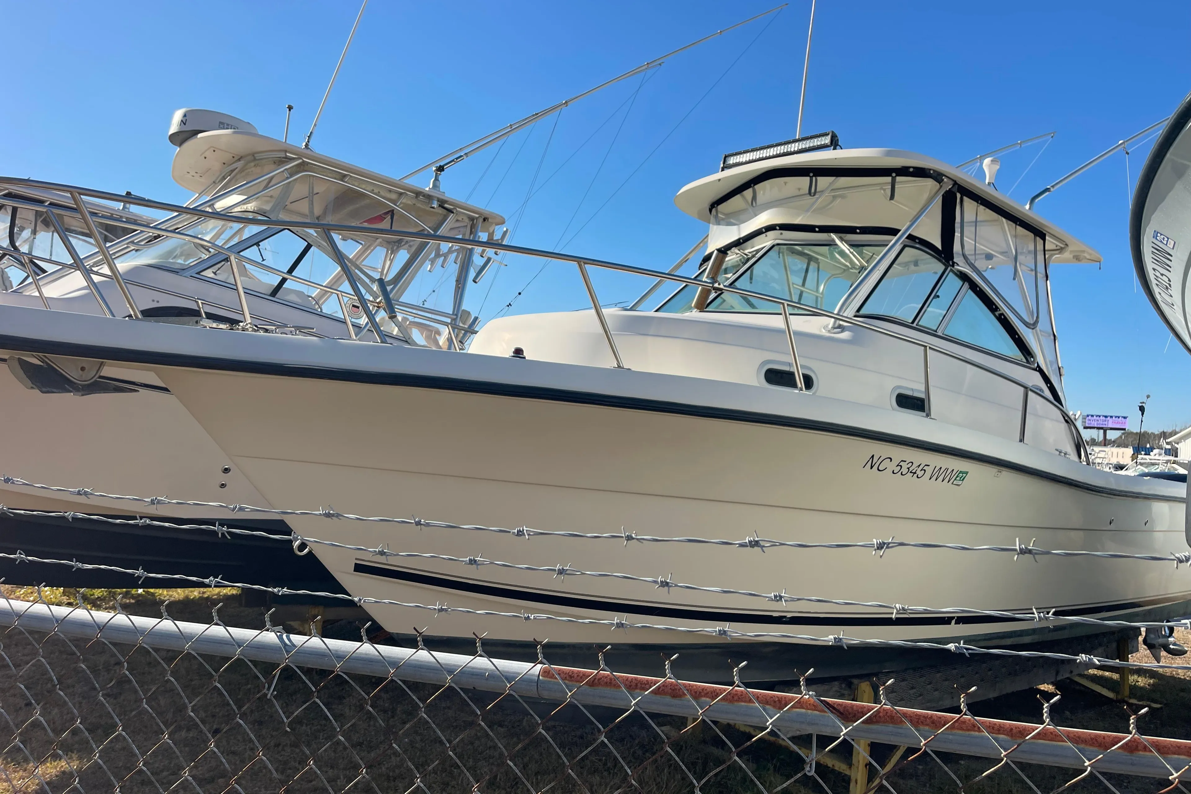 2003 Pursuit 2870 Walkaround boat displayed behind a fence under clear blue sky.