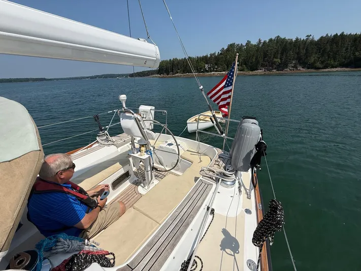 Dawn Treader Yacht Photos Pics Man relaxing on a 2005 Tartan 3700 sailboat, American flag waving, scenic coastal view.