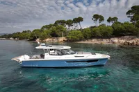 2023 Nimbus W11 yacht cruising near a scenic, tree-lined coastline under a partly cloudy sky.