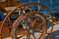 Wooden steering wheel on 1929 Camper & Nicholsons J Class yacht, sailing on blue ocean.