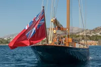 1929 Camper & Nicholsons J Class yacht with red ensign flag sailing on blue waters.