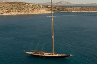 1929 Camper & Nicholsons J Class yacht sailing in clear blue waters near rocky coastline.