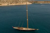 1929 Camper & Nicholsons J Class yacht sailing in clear blue waters near rocky coastline.