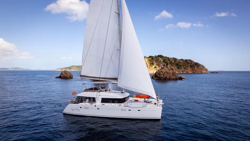 Copper Penny Yacht Photos Pics Sailing catamaran Lagoon 560, 2011 model, cruising near rocky island under clear blue sky.