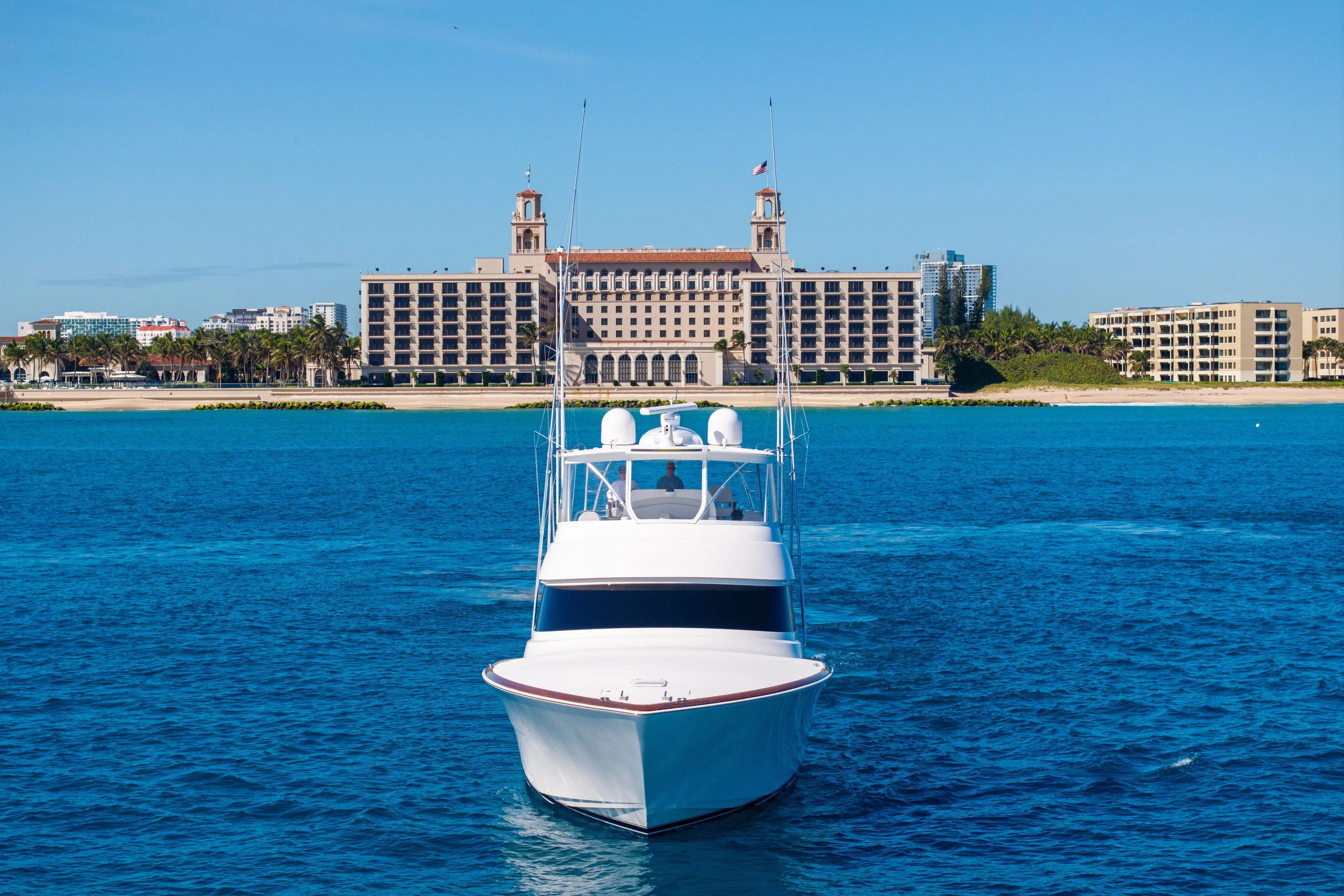 2025 Viking 64 Convertible yacht on blue water with beachfront hotel in background.