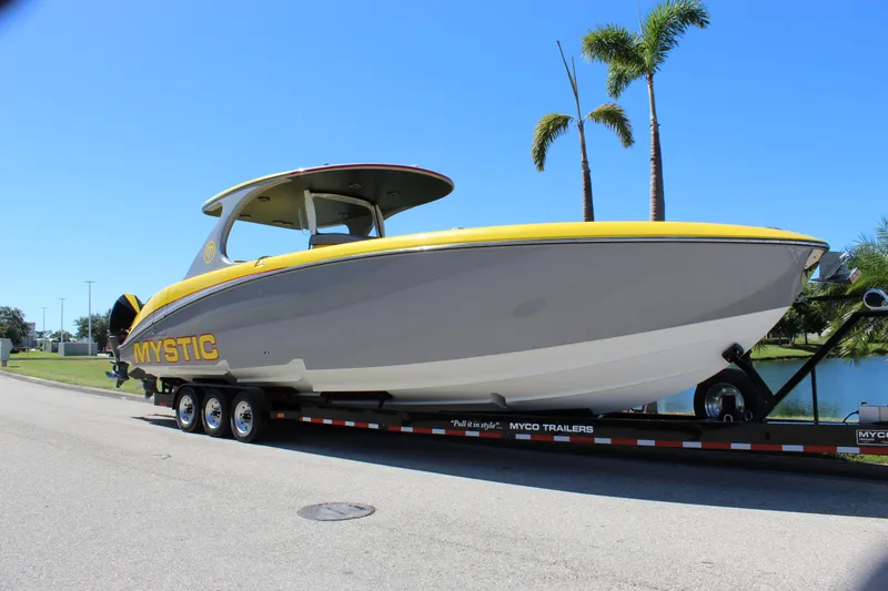  Yacht Photos Pics 2021 Mystic M4200 boat on trailer, yellow and gray design, parked near palm trees.