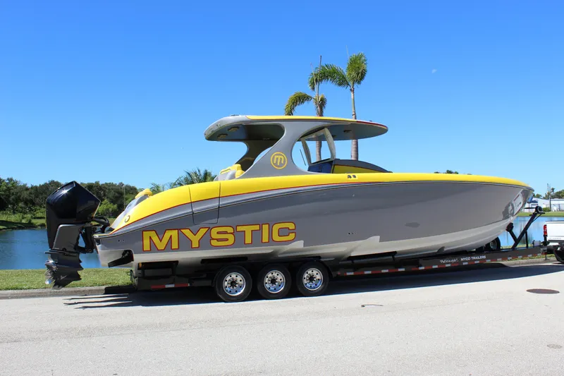  Yacht Photos Pics 2021 Mystic M4200 boat on trailer, yellow and gray design, parked by a lake.
