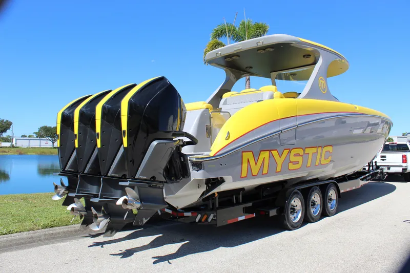  Yacht Photos Pics 2021 Mystic M4200 powerboat with four engines on a trailer, parked by a lake.