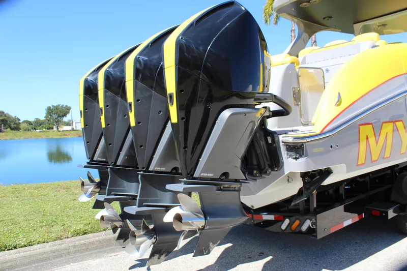  Yacht Photos Pics 2021 Mystic M4200 boat with four powerful outboard engines, docked by a serene lake.