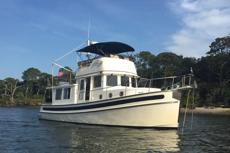 Egret Yacht Photos Pics 2005 Nordic Tug 37 Flybridge boat on calm water near a wooded shoreline.