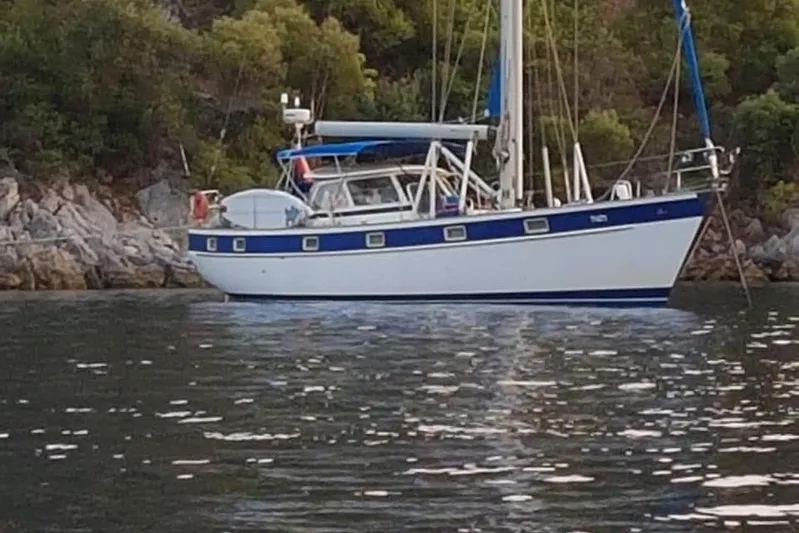  Yacht Photos Pics 1986 Hallberg-Rassy 49 sailboat anchored near rocky shoreline with lush greenery.