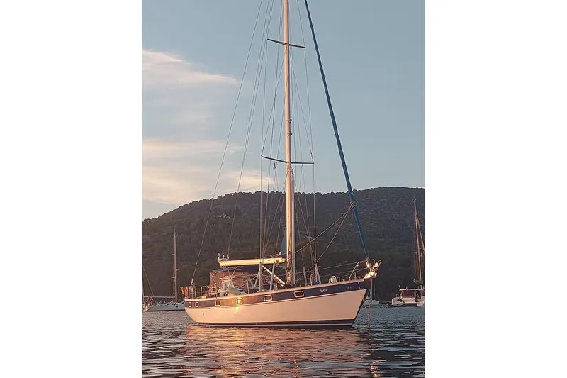  Yacht Photos Pics 1986 Hallberg-Rassy 49 sailboat anchored at sunset with scenic mountain backdrop.