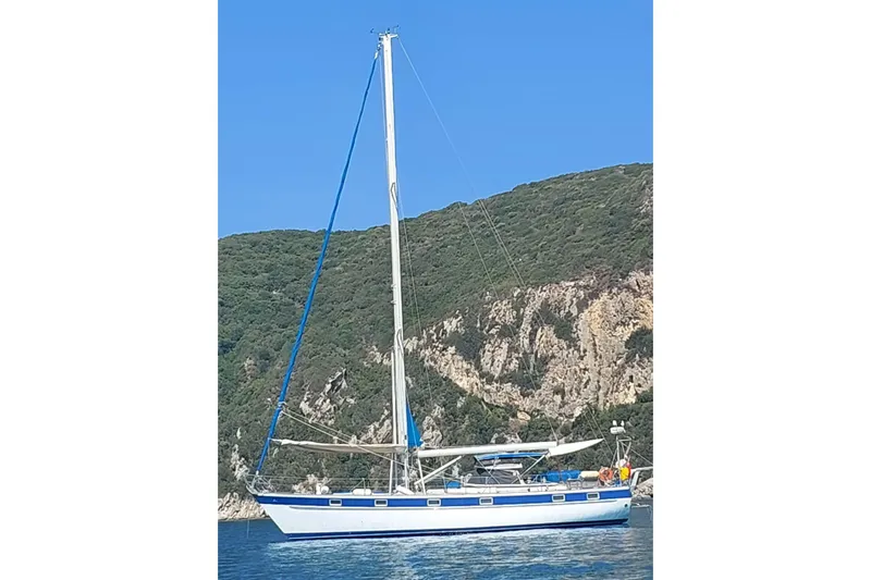  Yacht Photos Pics 1986 Hallberg-Rassy 49 sailboat anchored near rocky coastline under clear blue sky.