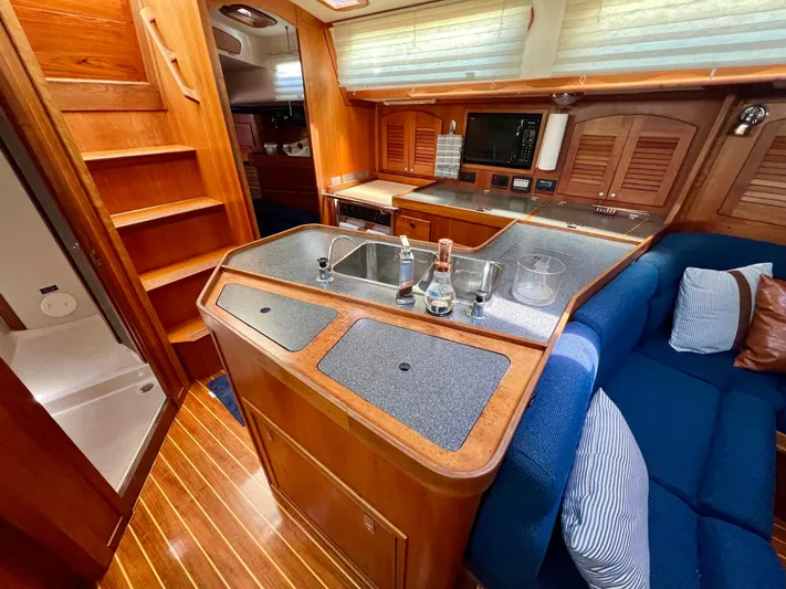 Vela Dare II Yacht Photos Pics 1999 Sabre 402 yacht interior with wooden cabinetry, kitchen sink, and blue seating.