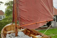Wooden sailboat with red sail, Custom Snipa model, 2023, docked in a garden setting.