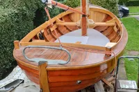 Wooden sailboat "Snipa" 2023 model, on land, surrounded by greenery and residential area.