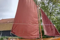 Wooden sailboat with red sails, Custom Snipa model, 2023, displayed outdoors.