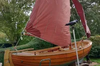 Wooden sailboat with red sails, Custom Snipa model, 2023, displayed on land with greenery.