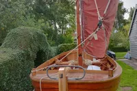 Wooden sailboat with red sail, Custom Snipa model, 2023, in a garden setting.