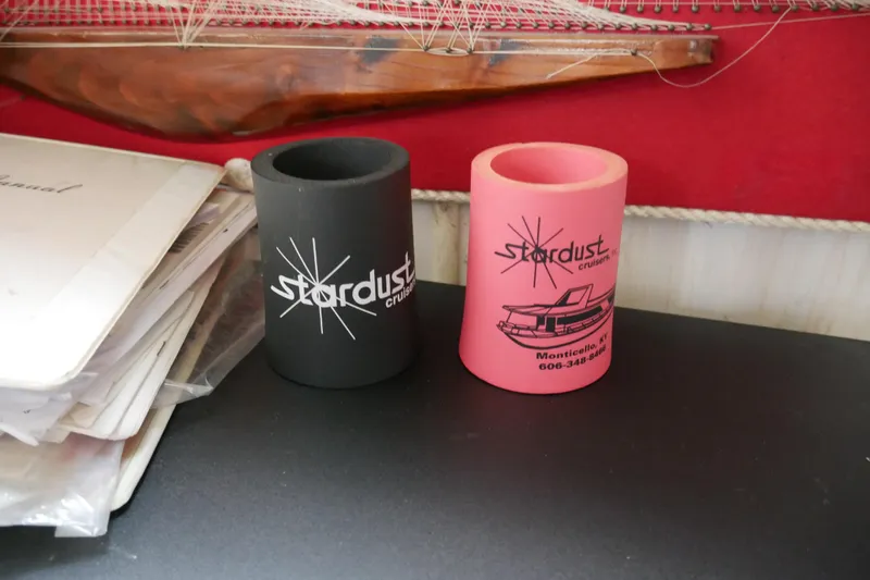  Yacht Photos Pics Two Stardust Cruiser can holders, black and pink, on a table with documents.
