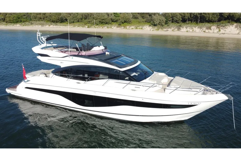 B III Yacht Photos Pics 2021 Princess S62 yacht cruising on calm waters near a sandy shoreline.