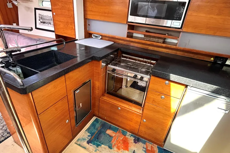 Scacciapensieri Yacht Photos Pics 2008 Hanse 470e yacht kitchen with wood cabinetry, black countertops, and modern appliances.