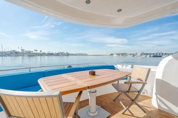 Zenyatta Yacht Photos Pics Sunseeker Manhattan 60 yacht deck with wooden table and chairs, overlooking serene waters.