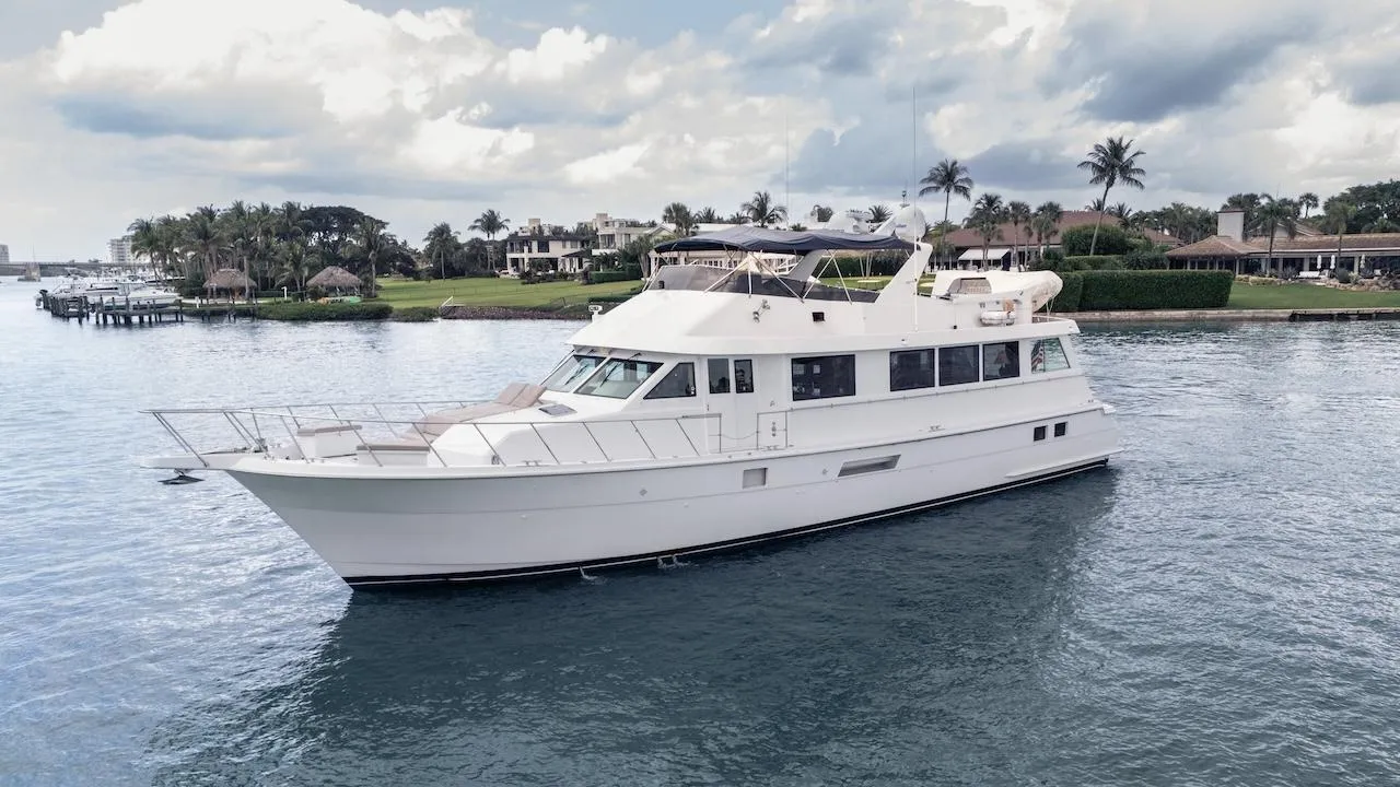 1998 Hatteras 74 Sport Deck Motor Yacht cruising on calm waters near a tropical shoreline.