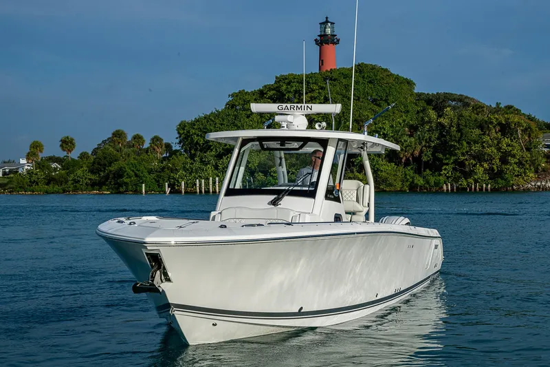 Pigasus Yacht Photos Pics 2024 Pursuit S 328 Sport boat cruising near a lighthouse and lush greenery.