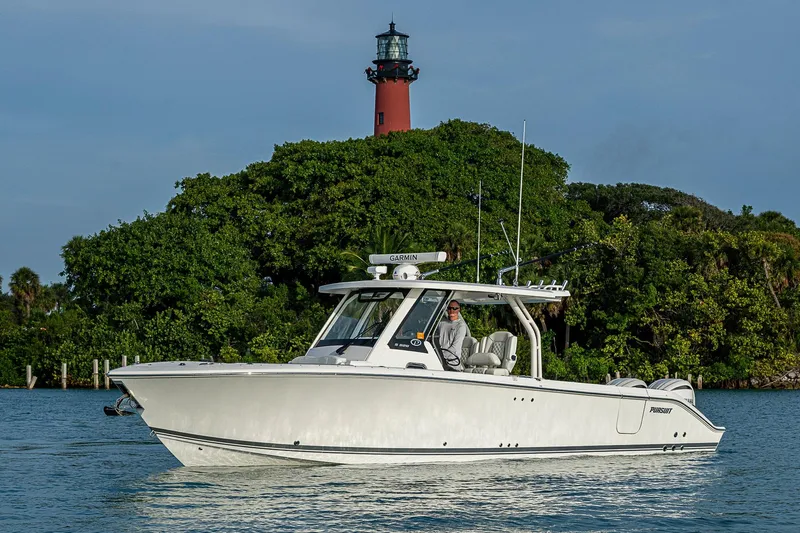 Pigasus Yacht Photos Pics 2024 Pursuit S 328 Sport boat cruising near a lighthouse and lush greenery.