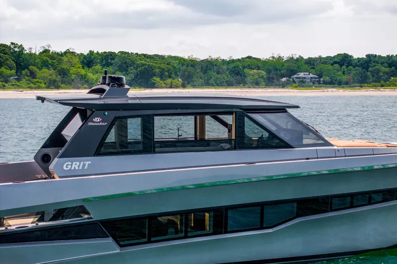 Grit Yacht Photos Pics 2025 Steeler Bronson 67 Beachclub yacht on water, sleek design, lush shoreline background.