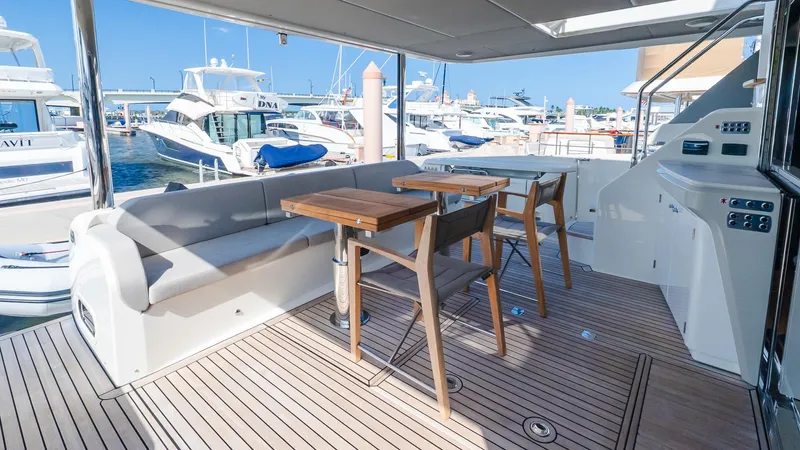 Available Now Yacht Photos Pics Outdoor seating area on 2024 Absolute 68 NAVETTA yacht, featuring wooden tables and marina view.