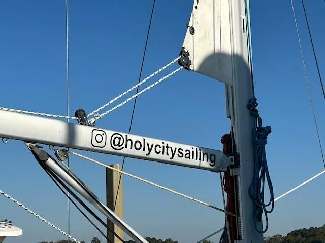 Golden Handcuffs Yacht Photos Pics Beneteau 373 sailboat mast with "@holycitysailing" Instagram handle, clear blue sky background.
