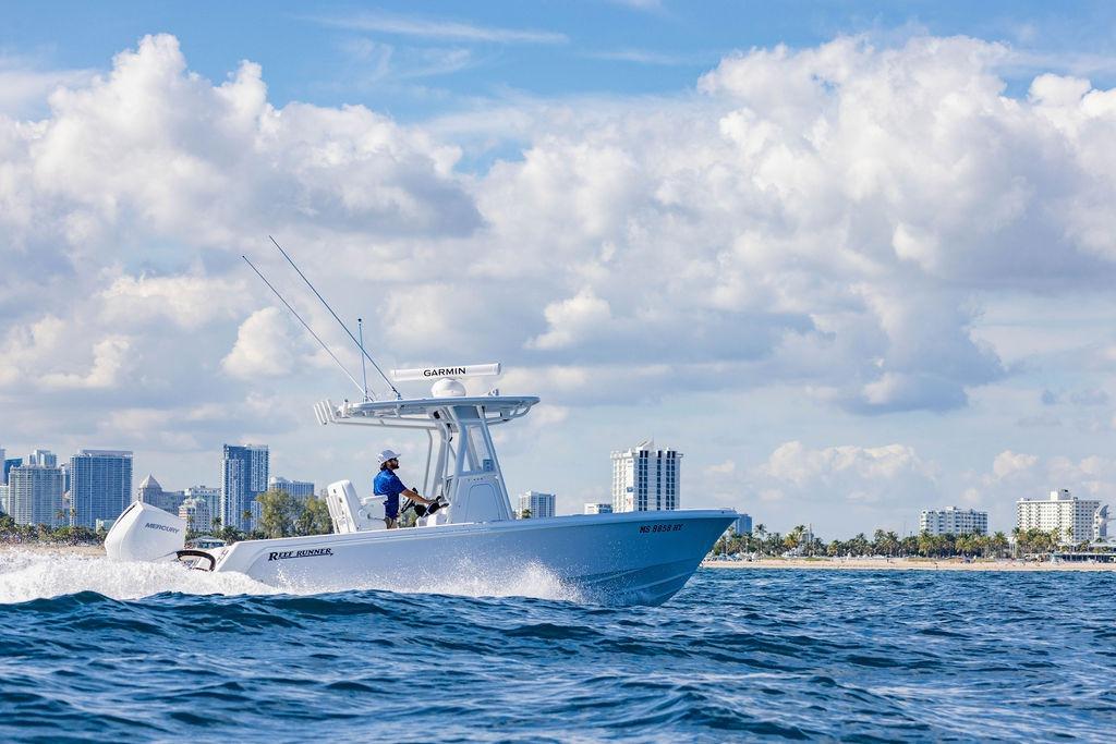 2024 Reef Runner 230 Open boat cruising near city skyline under cloudy sky.