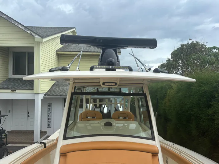  Yacht Photos Pics 2014 Scout 350 LXF boat with radar, parked near a house under cloudy skies.